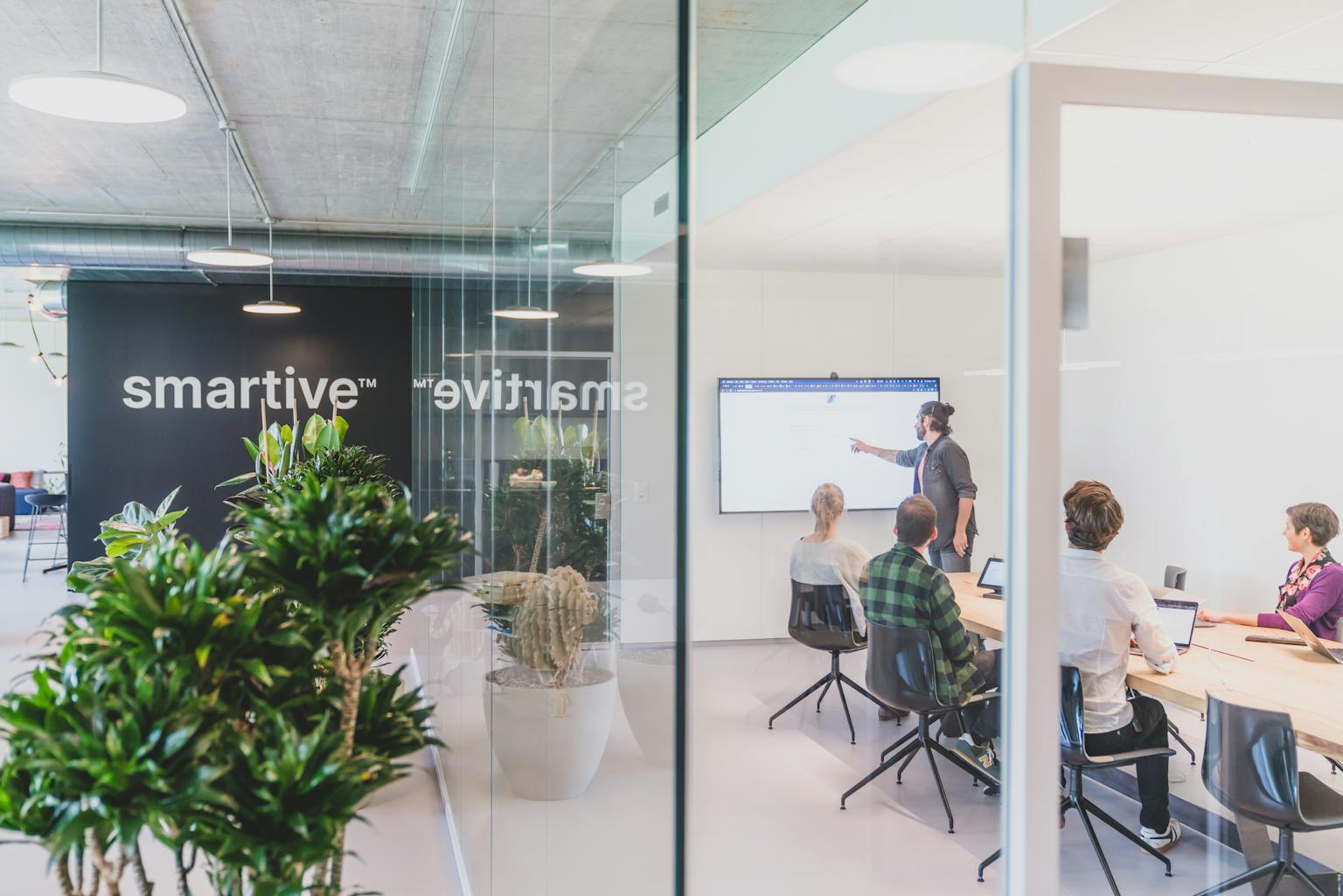 Blick ins smartive Büro mit Logo an der Wand. Mitarbeiter haben ein Meeting im Konferenzraum.